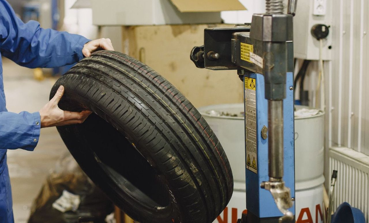 Mechanic in blue uniform examining a tire in an automotive garage.